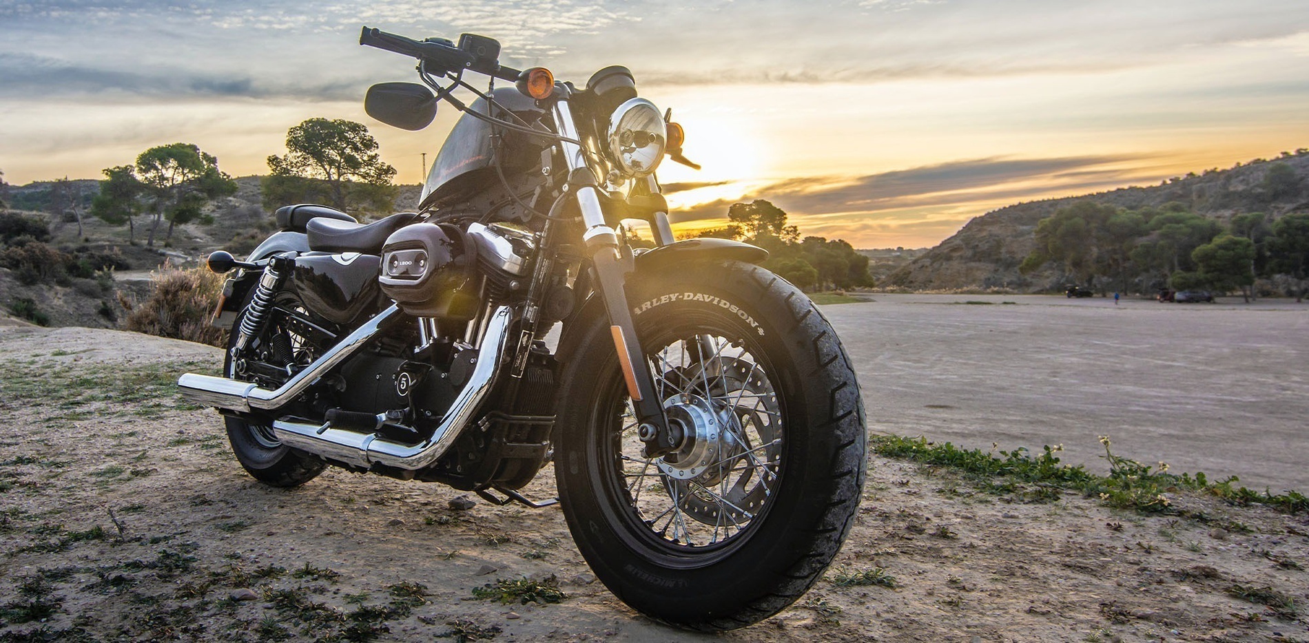 una motocicleta harley davidson está estacionada en un campo de arena al atardecer