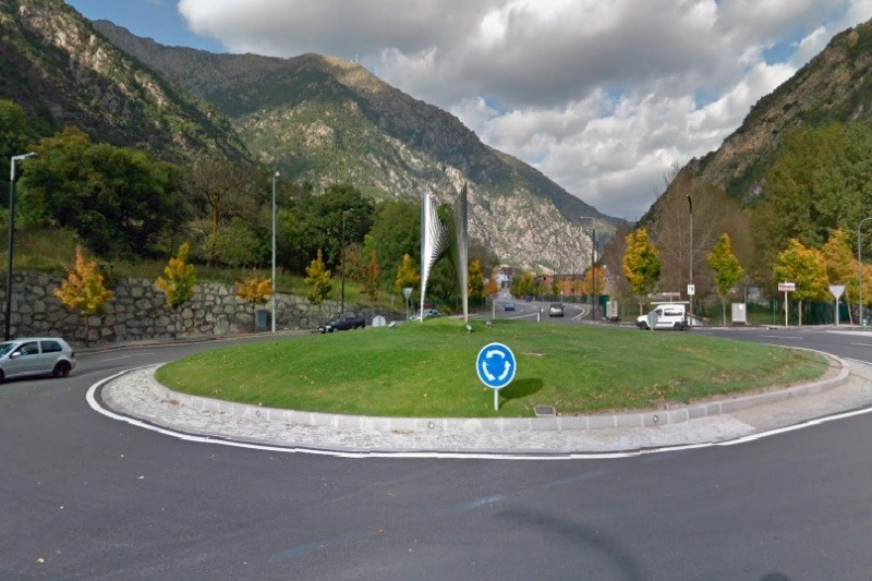 una rotonda rodeada de hierba y coches con montañas en el fondo