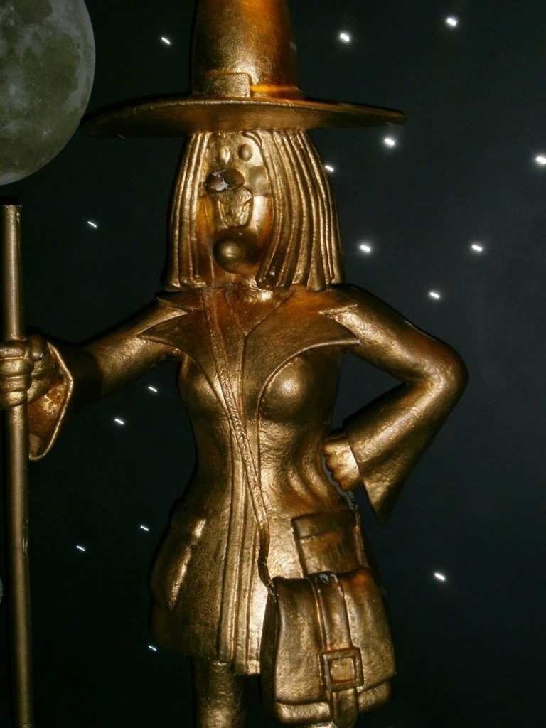 una estatua de una bruja dorada con un sombrero y un bastón