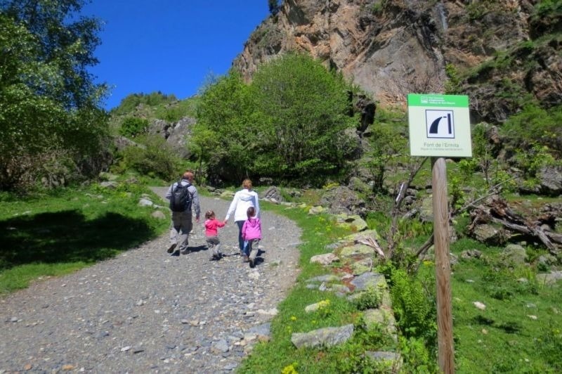 un hombre y dos niños caminan por un camino de tierra junto a una señal que dice fort de girona