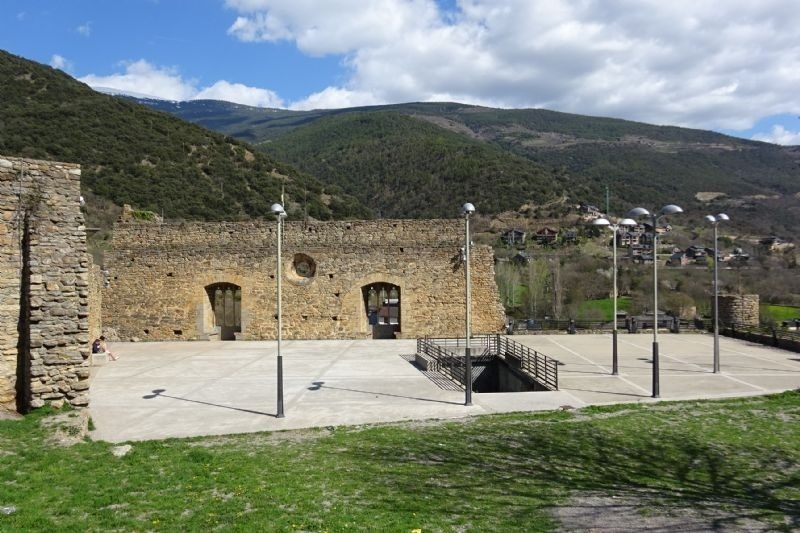 a man walking in front of a stone building with mountains in the background