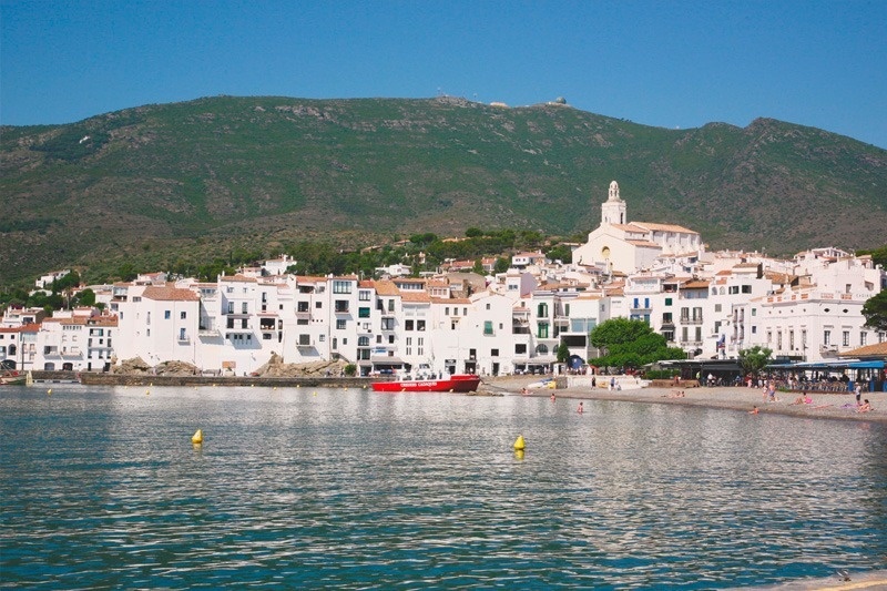 a small white town sits on the shore of a body of water