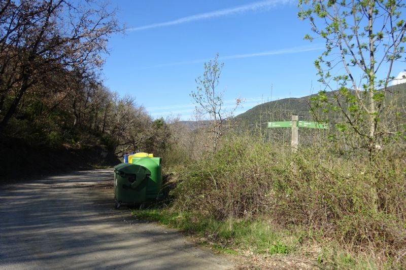 un bote de basura verde está al costado de un camino de tierra
