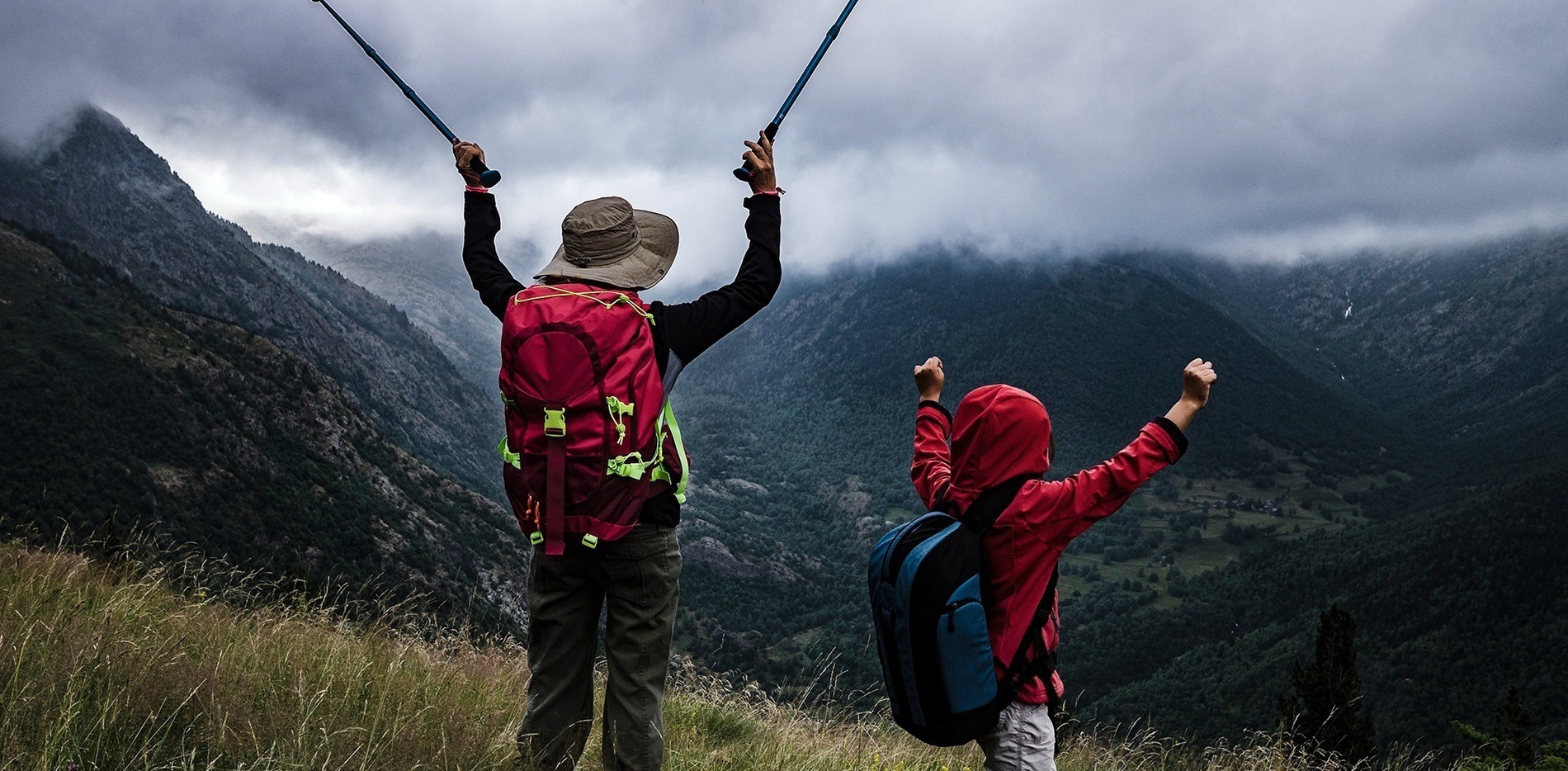 un hombre con una mochila roja y un niño con una chaqueta con capucha levantan sus manos en el aire