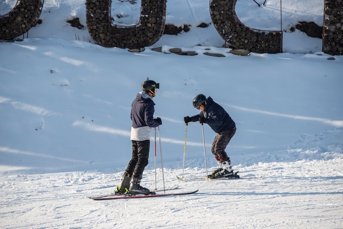 dos esquiadores se paran en la nieve frente a una gran letra u