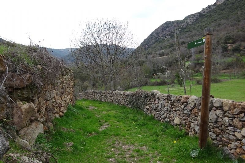 a stone wall along a path with a sign pointing to the right
