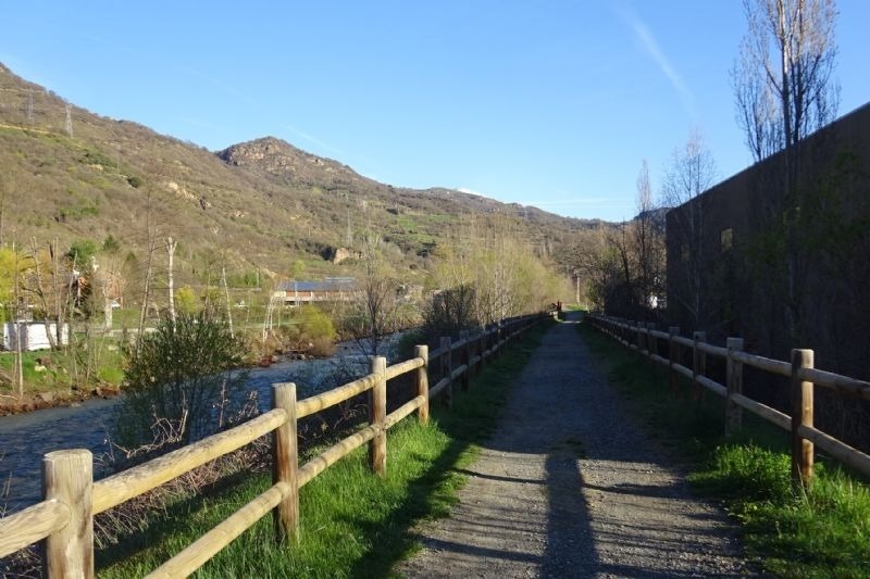 un camino de tierra con una cerca de madera y un río en el fondo