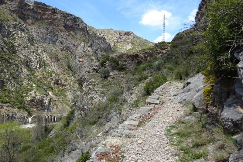 un camino de tierra en una montaña con un puente en el fondo