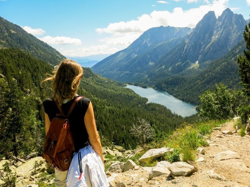 una mujer con una mochila mirando un lago en las montañas
