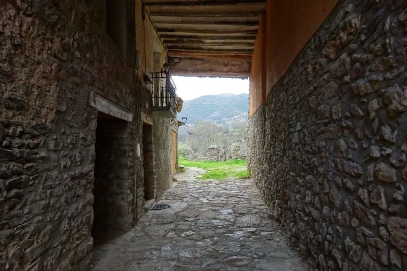 a stone alleyway with a balcony and mountains in the background