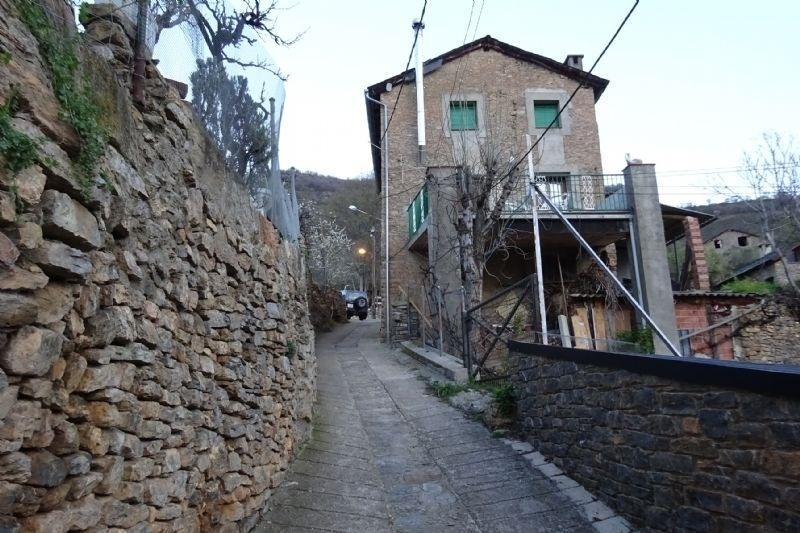a stone wall along the side of a road leads to a building with a balcony