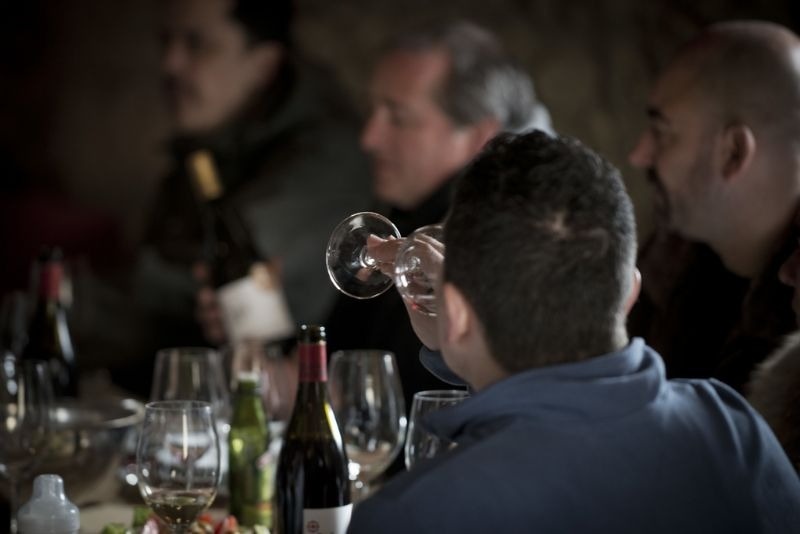 a man is drinking from a wine glass with a bottle of wine in the background
