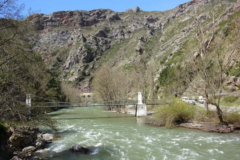 un puente colgante sobre un río con montañas en el fondo