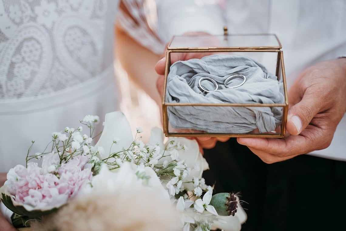a bride and groom hold their wedding rings in a glass box