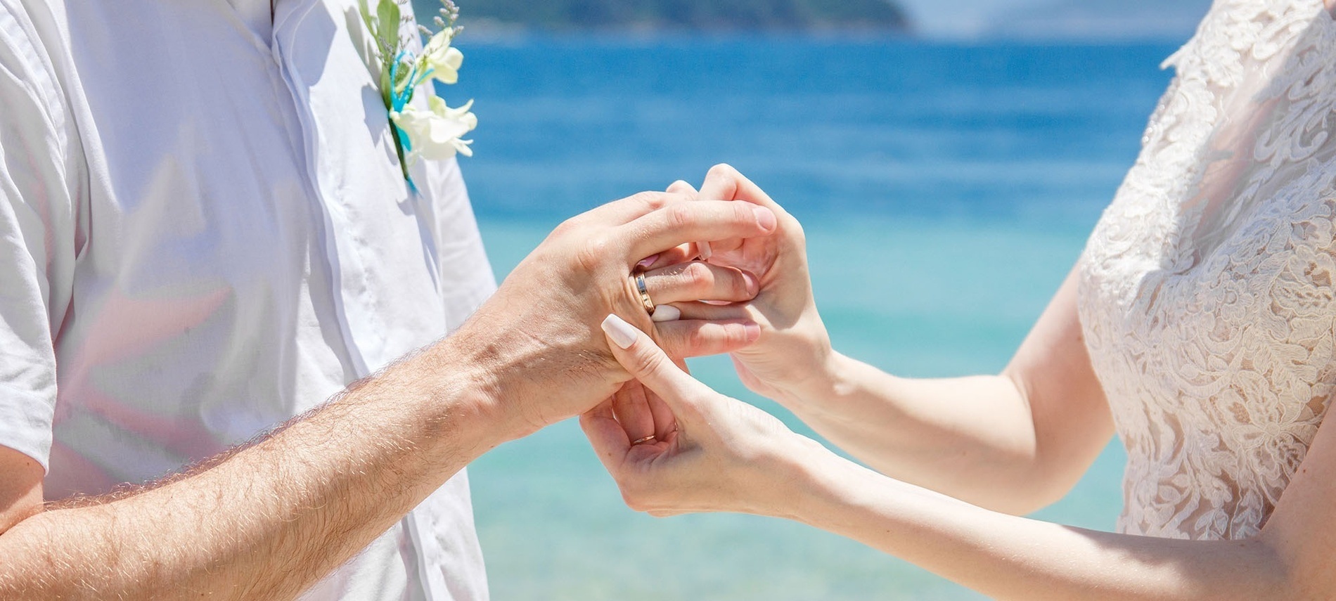 una novia y un novio parados en la playa con anillos de boda en primer plano