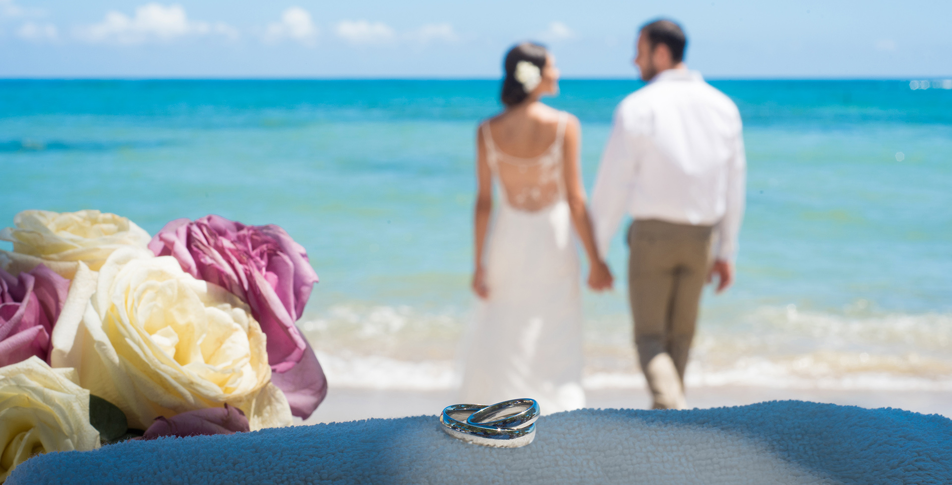a bride and groom walking on the beach with wedding rings in the foreground