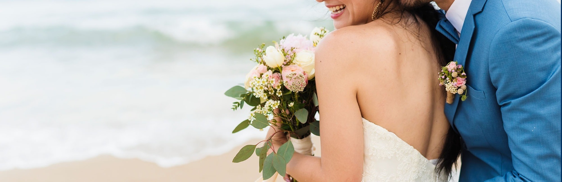 una novia y un novio parados en la playa con anillos de boda en primer plano