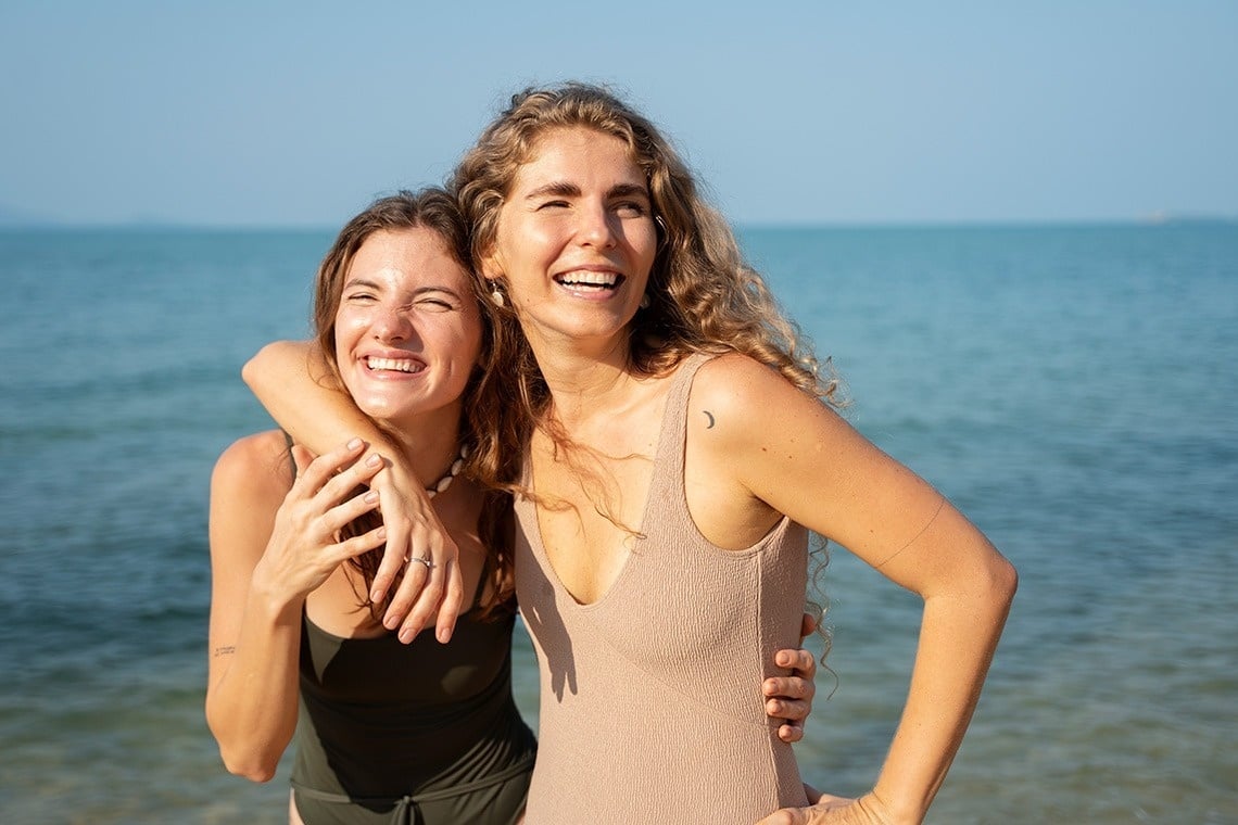 dos mujeres se abrazan en la playa y sonríen