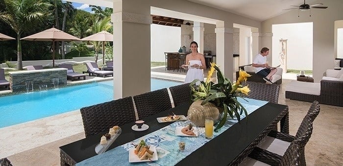 una mujer sostiene un plato de comida en una mesa de comedor junto a una piscina .