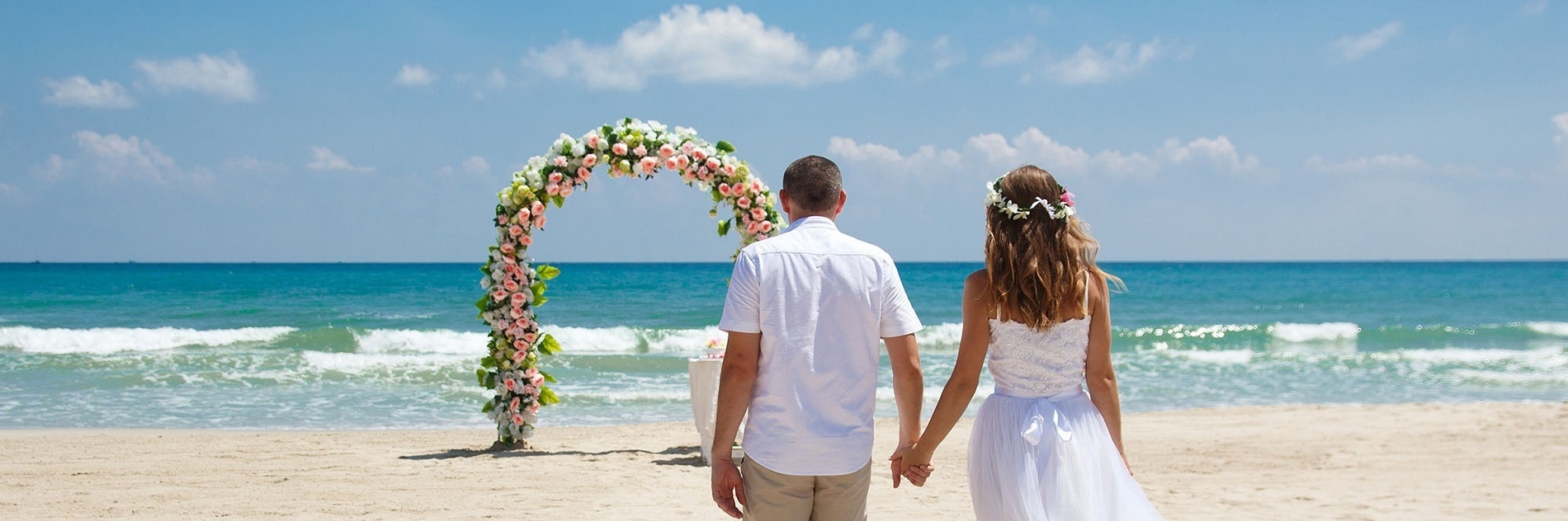 a bride and groom walking on the beach with wedding rings in the foreground