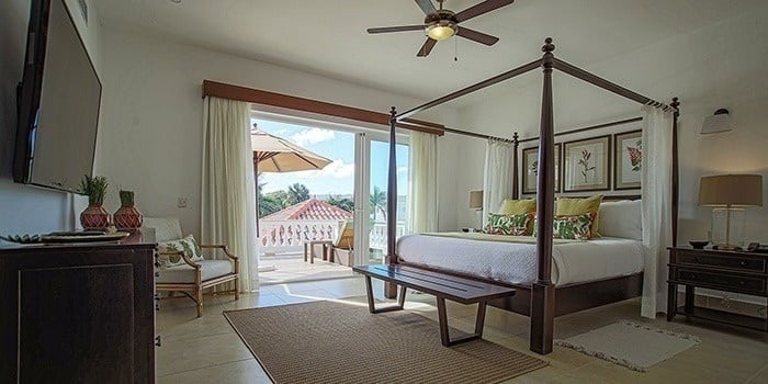 a bedroom with a canopy bed , a flat screen tv , a bench and a balcony .
