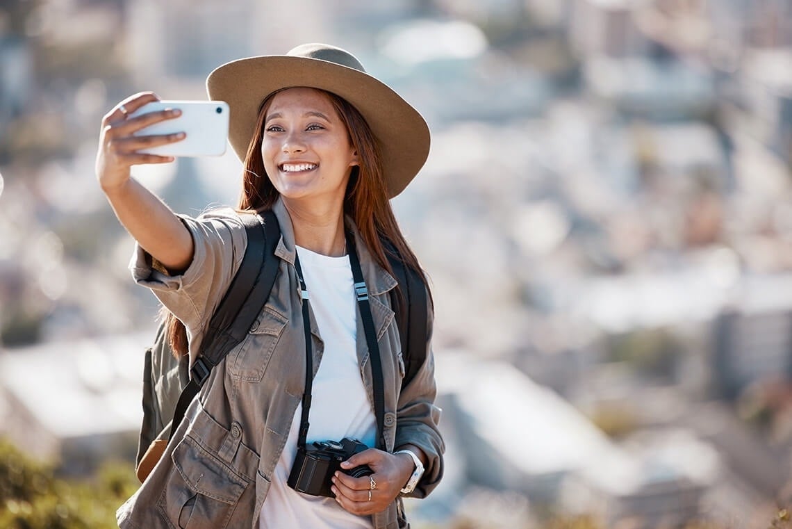 una mujer con sombrero y mochila toma un selfie con su teléfono