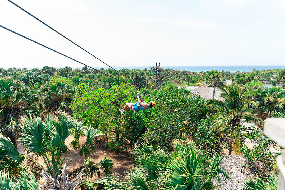 Persona en tirolesa sobre un exuberante paisaje tropical y el océano, ideal paraLHVC Resorts: Corpo.