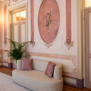 a couch in front of a pink wall with a painting of a woman on it