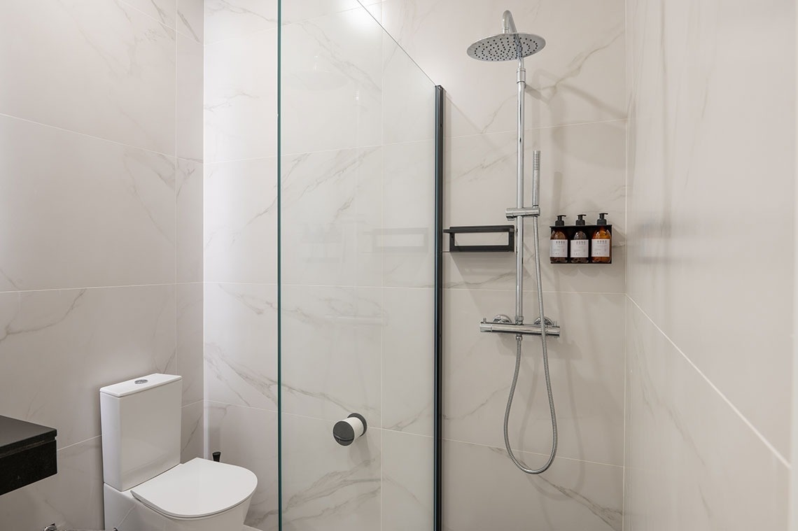 a bathroom with a toilet and shower with bottles on the wall