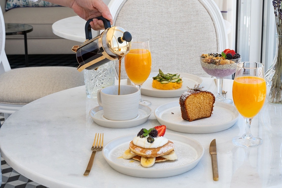 una persona vierte café en una taza sobre una mesa con platos de comida