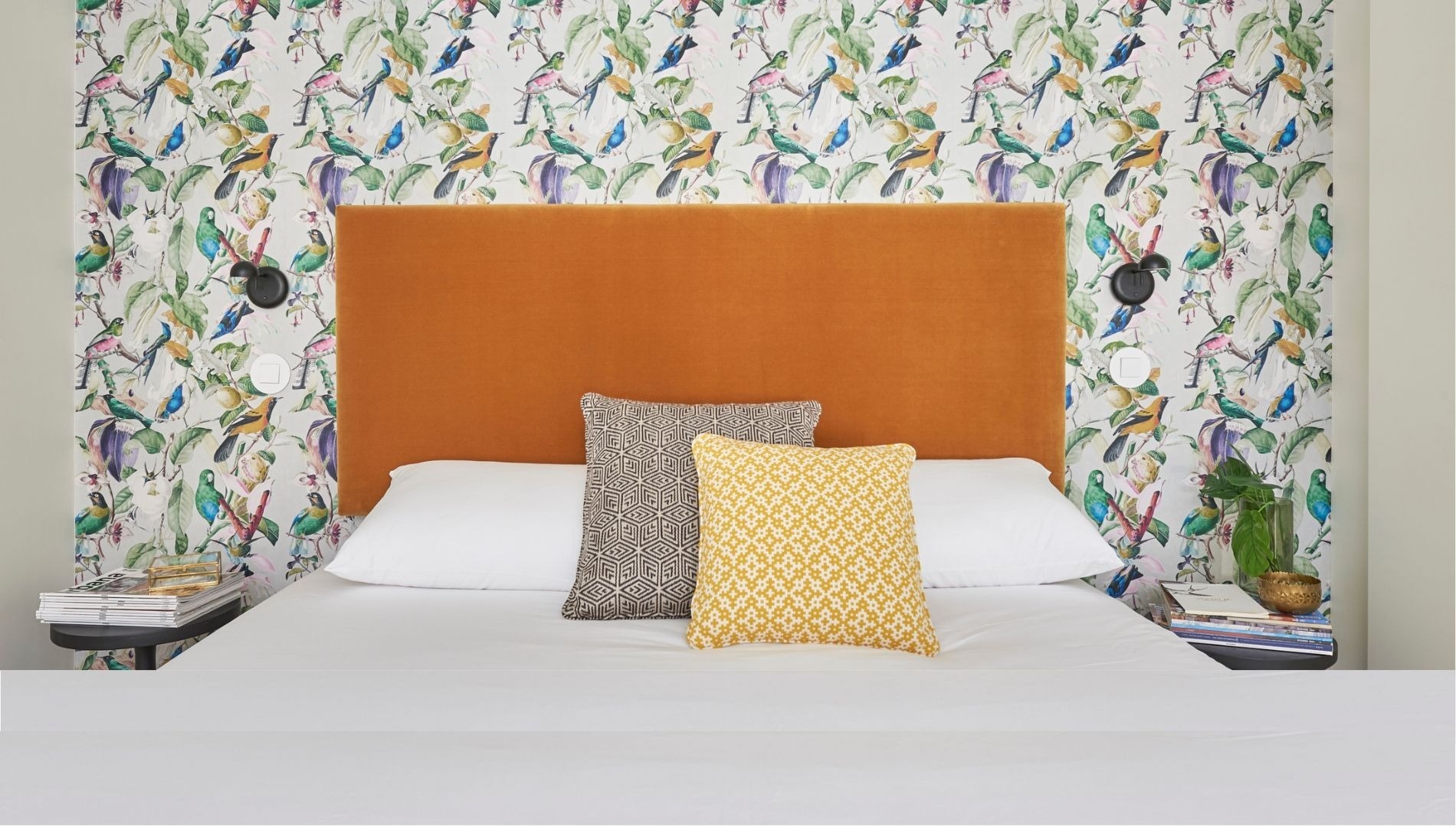 a bed with a headboard and pillows in front of a wall with birds on it