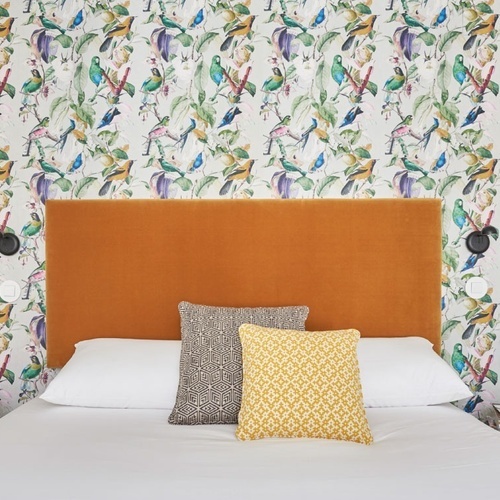 a bed with a headboard and pillows in front of a wall with birds on it