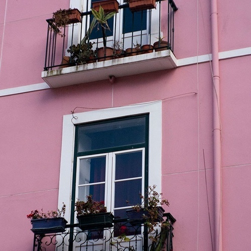 um prédio rosa com duas varandas cheias de vasos de plantas