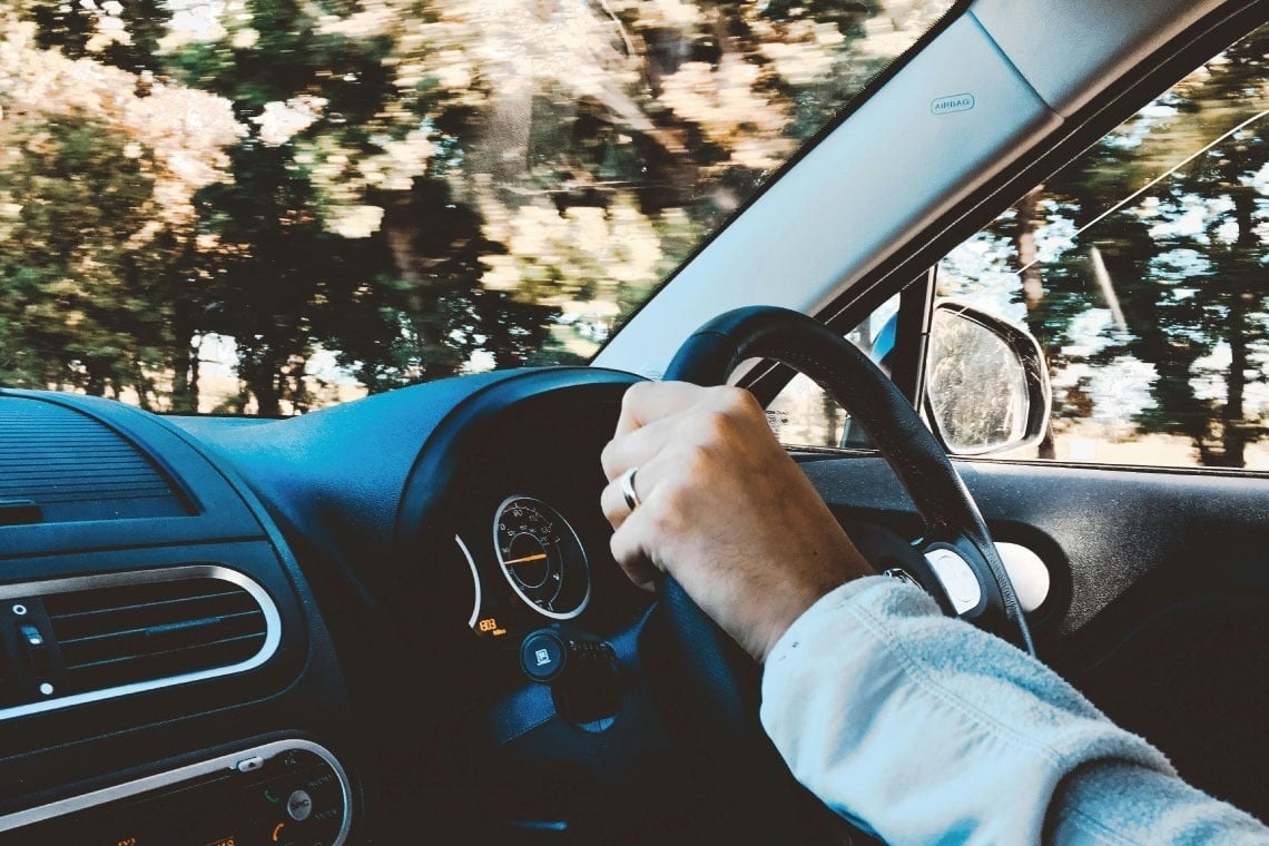 una persona sostiene el volante de un automóvil mientras conduce por la carretera