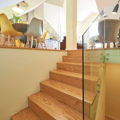 a wooden staircase with a glass railing and yellow chairs