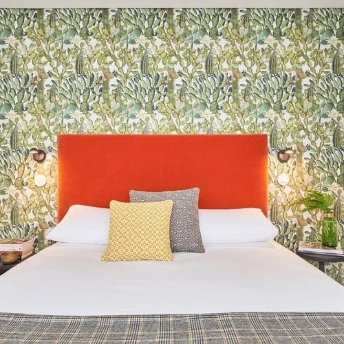 a bed with a red headboard in front of a wall with cactus wallpaper