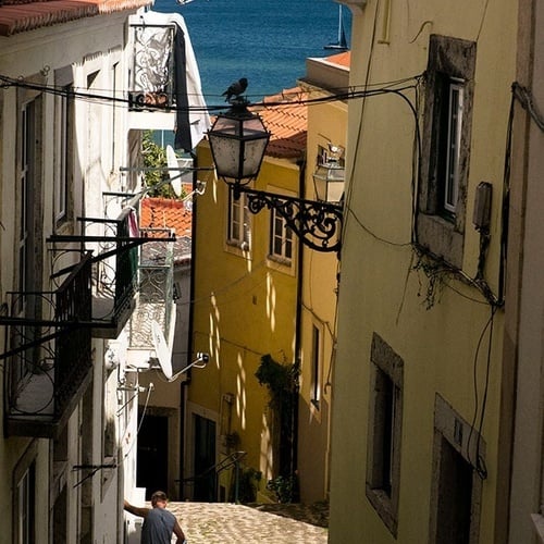 um homem caminha por uma rua de paralelepípedos com o oceano ao fundo