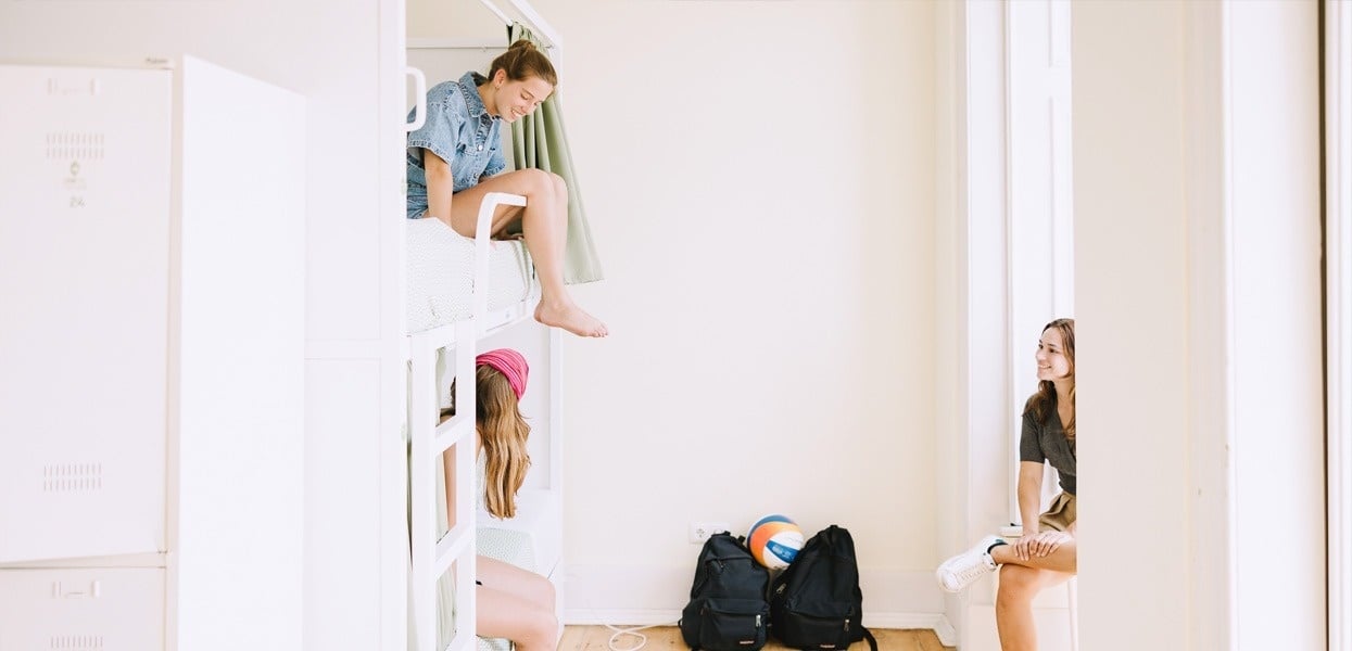 tres chicas se sientan en una habitación con literas y mochilas