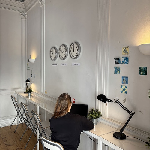 Espaço de trabalho de coworking em hotel para hóspedes com laptop, mesas e relógios de fusos horários.