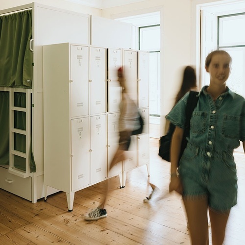 a woman in a green jumpsuit walks past a row of white lockers
