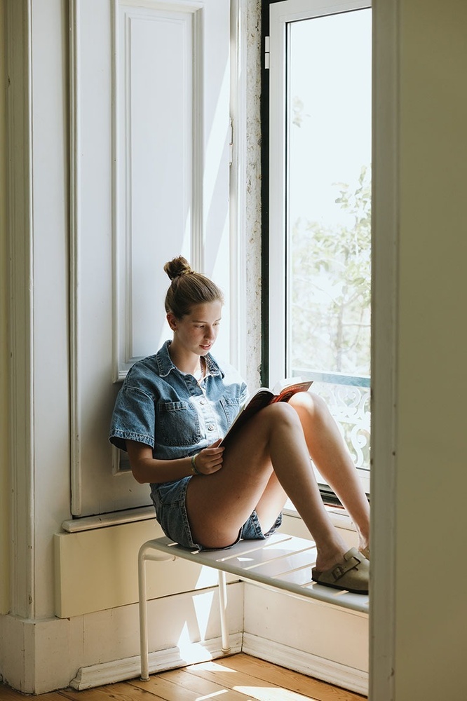 uma mulher sentada em uma janela lendo um livro