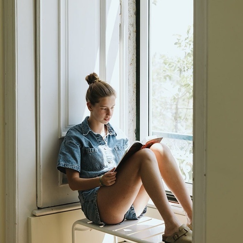a woman sits on a window sill reading a book