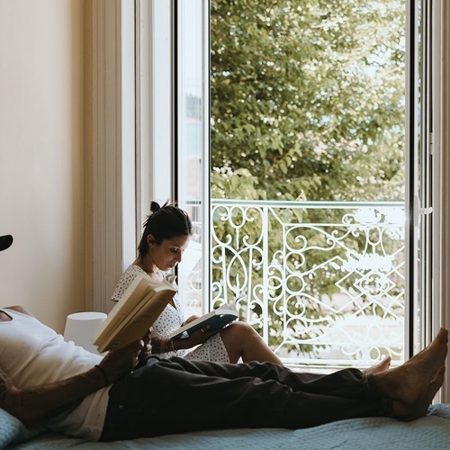 a man and a woman sit on a bed reading books