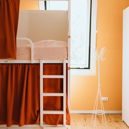 a bunk bed with orange curtains and a white ladder