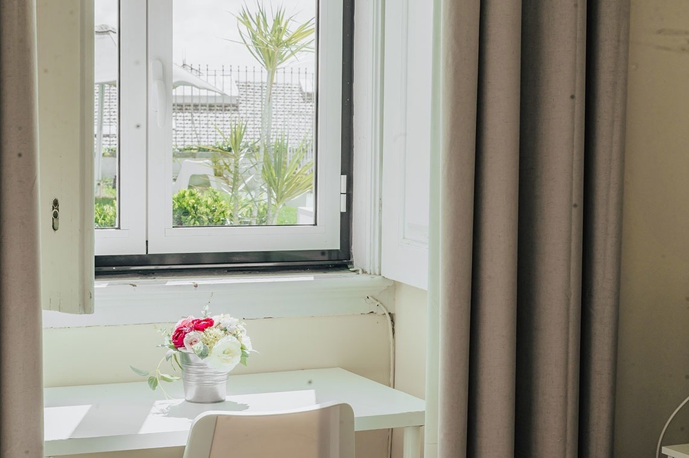 uma mesa branca com um vaso de flores na frente de uma janela