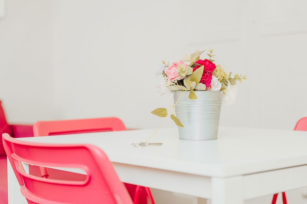 uma mesa branca com cadeiras cor de rosa e um vaso de flores