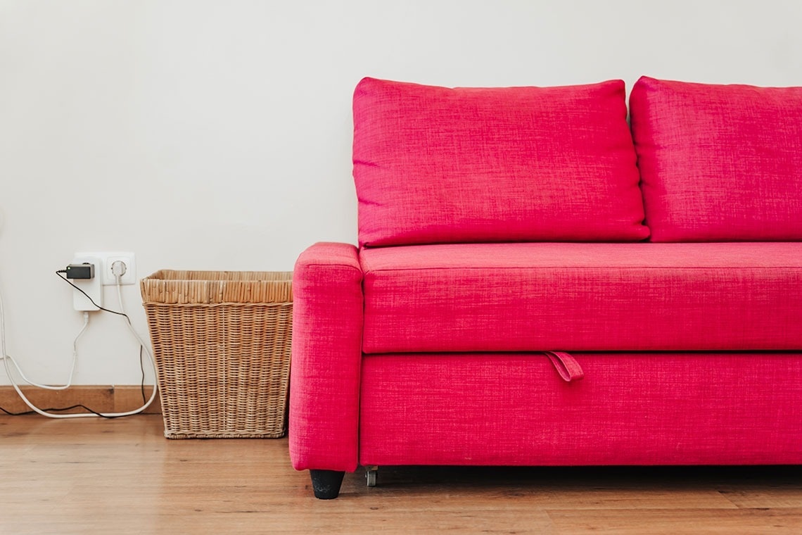 a pink couch sits next to a wicker basket