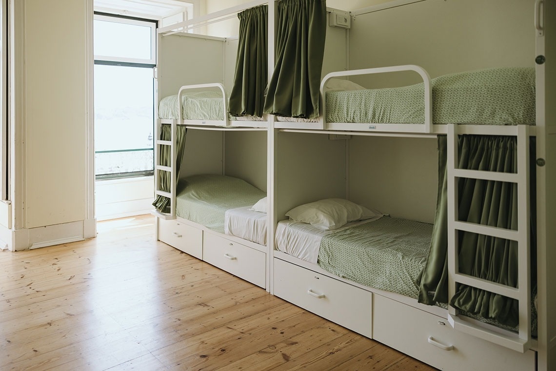 a row of bunk beds with green curtains and white sheets