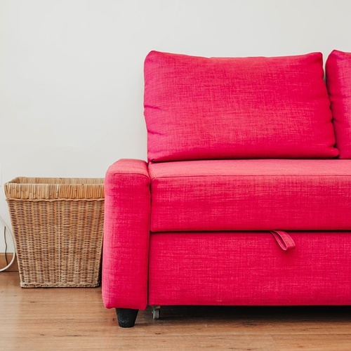 a pink couch sits next to a wicker basket