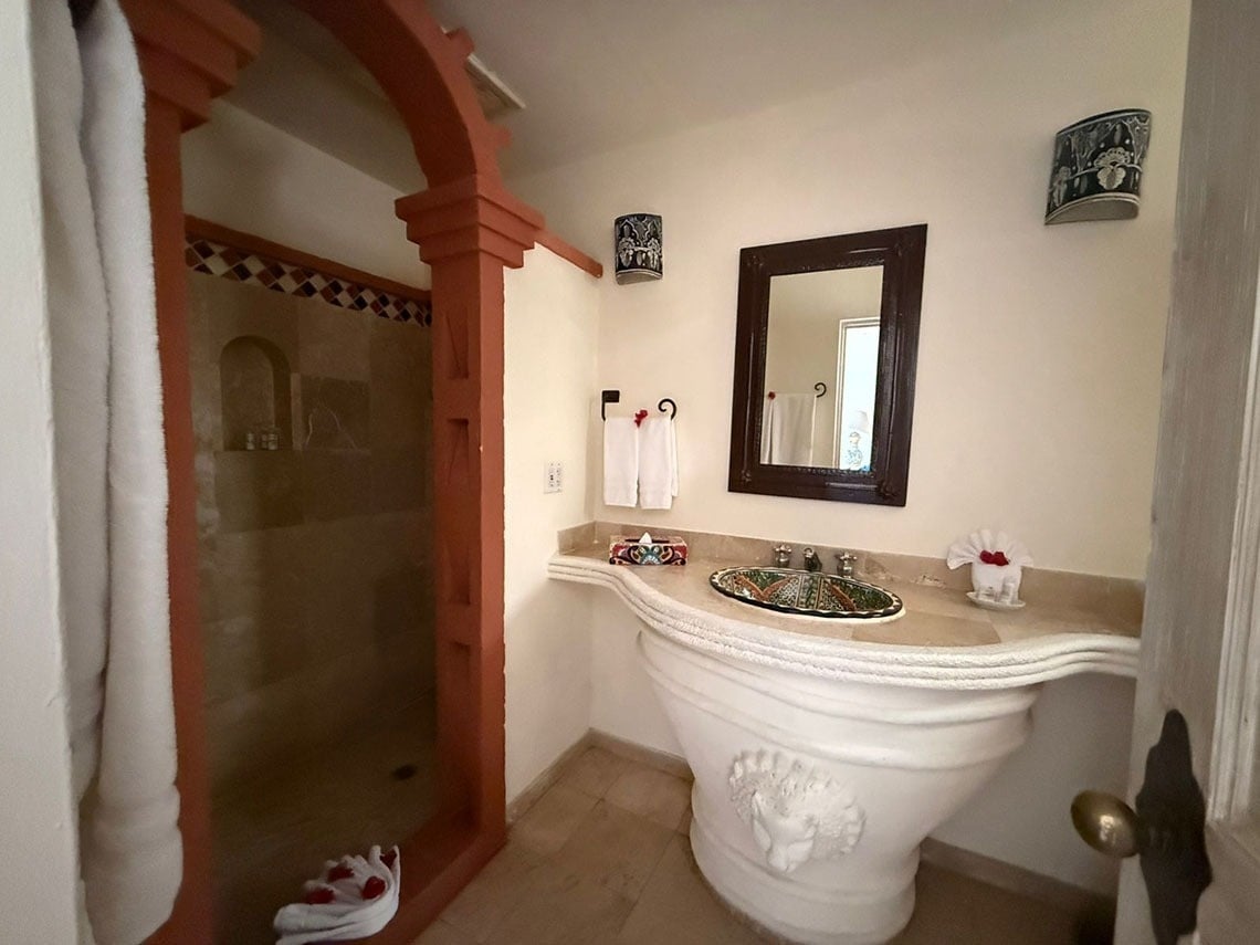 Un cuarto de baño de estilo mexicano con una ducha arqueada y un lavabo ornamentado con una base esculpida.